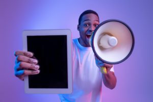 African Guy With Loudspeaker Holding Digital Tablet With Black Screen, Making Announcement